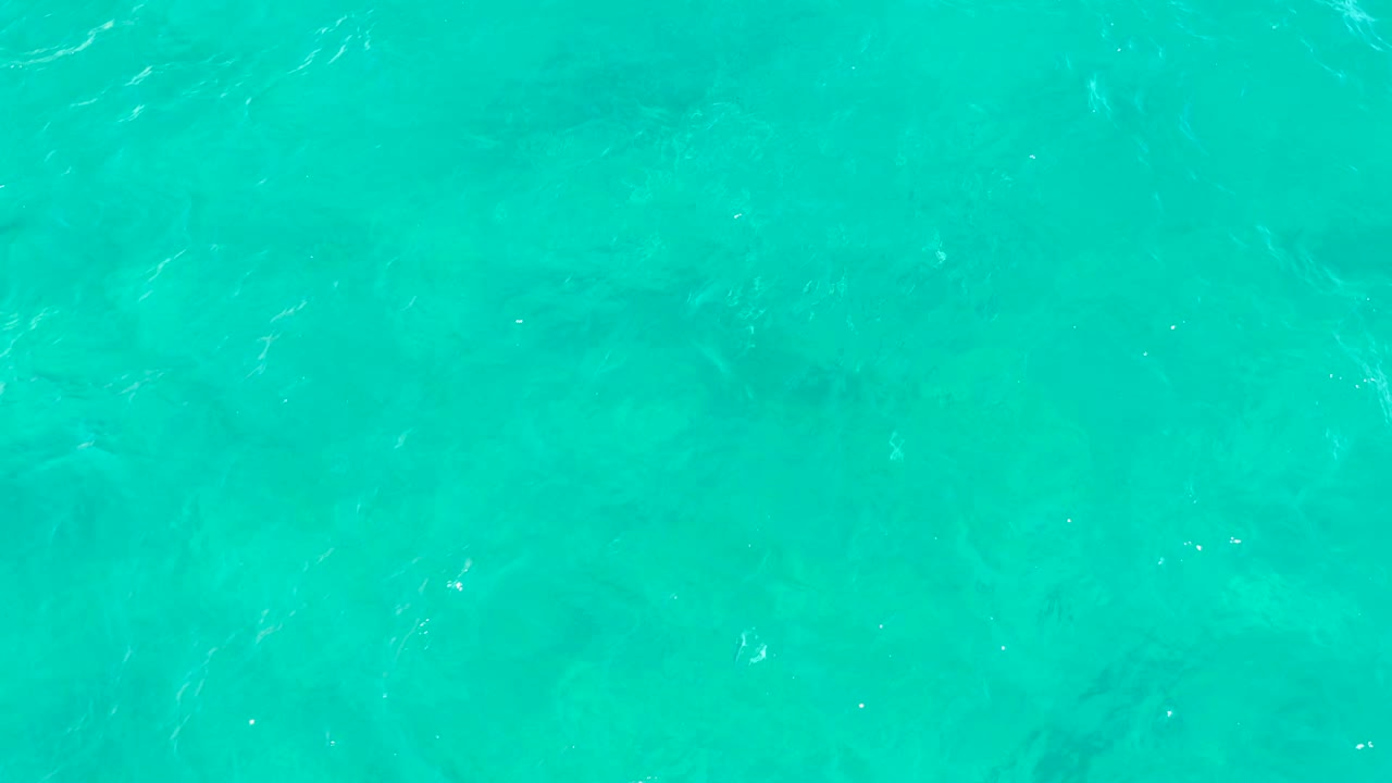 Clear turquoise water in East Cape, Baja California Sur, Mexico, with faint underwater seabed shapes, small surface ripples, and no visible people.