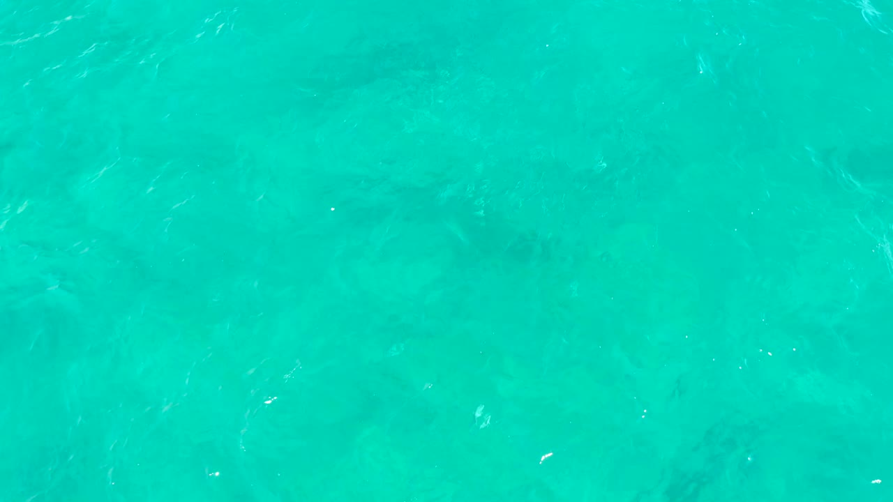 Blue green ocean surface in East Cape, Baja California Sur, Mexico, with a few tiny bubbles, pale reflected streaks, and no visible people.