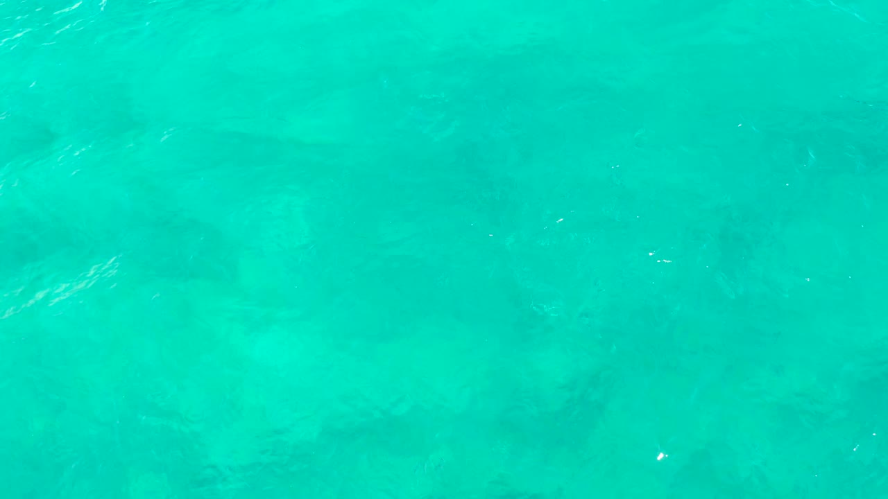 Turquoise shallow sea in East Cape, Baja California Sur, with brighter white highlights on the ripples and soft darker patches below the surface, no visible people.