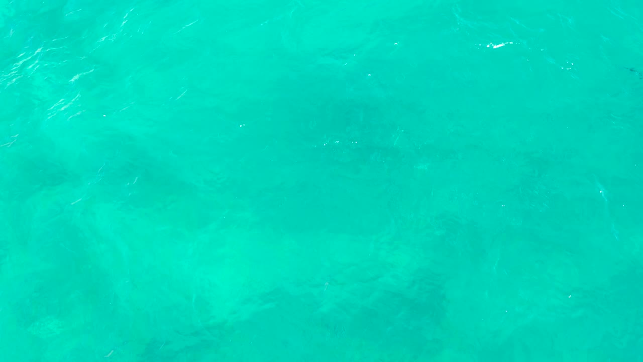 Clear turquoise ocean water in East Cape, Baja California Sur, with subtle underwater shapes and scattered reflective streaks across the surface, no visible people.
