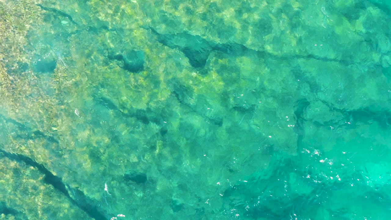 Shallow turquoise water in East Cape BCS Mexico shows submerged rocks and a diagonal dark crevice along the left side, with no visible people.