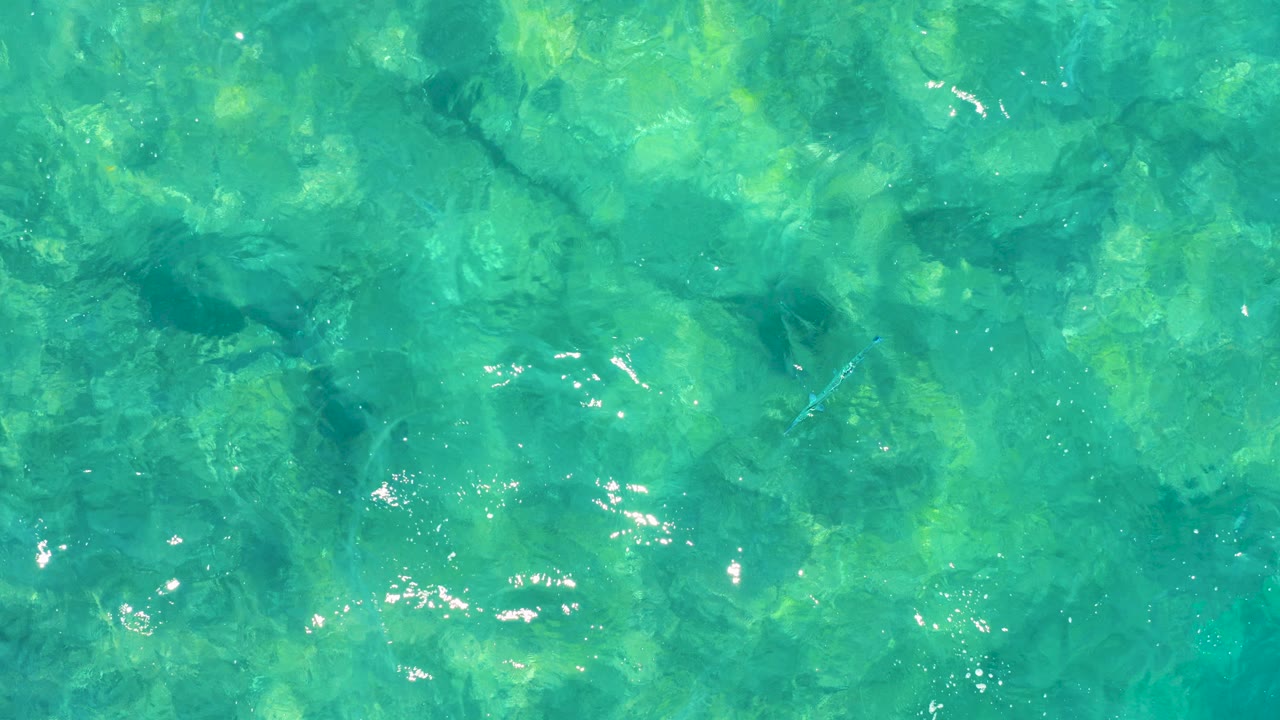 Clear turquoise ocean water in East Cape, Baja California Sur shows surface ripples, bright reflection spots, and green submerged texture with no visible people.