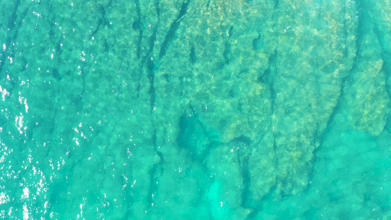 Turquoise ocean water over a visible seabed with sun glints.