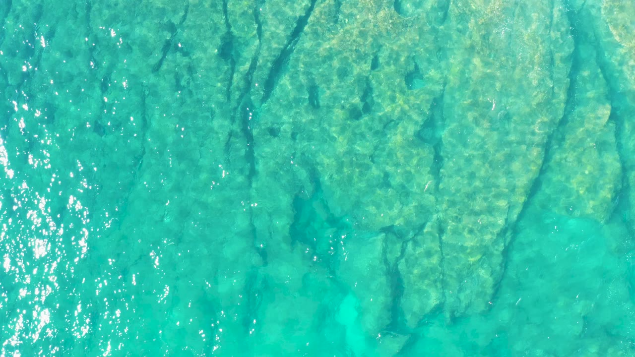 Aerial view of shallow turquoise water over pale underwater rock or coral forms in East Cape, Baja California Sur, with no visible people.