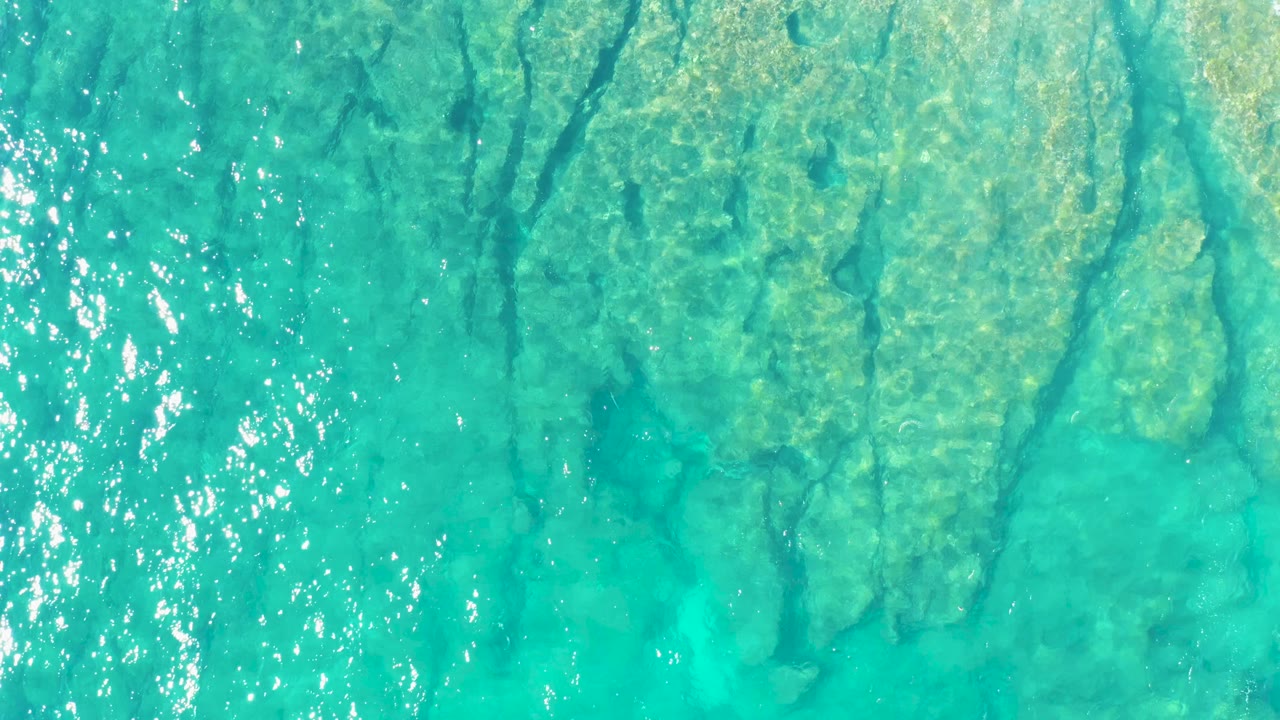 Sunlit ripples cross clear turquoise ocean water above a visible seabed in East Cape, Baja California Sur, with no visible people.