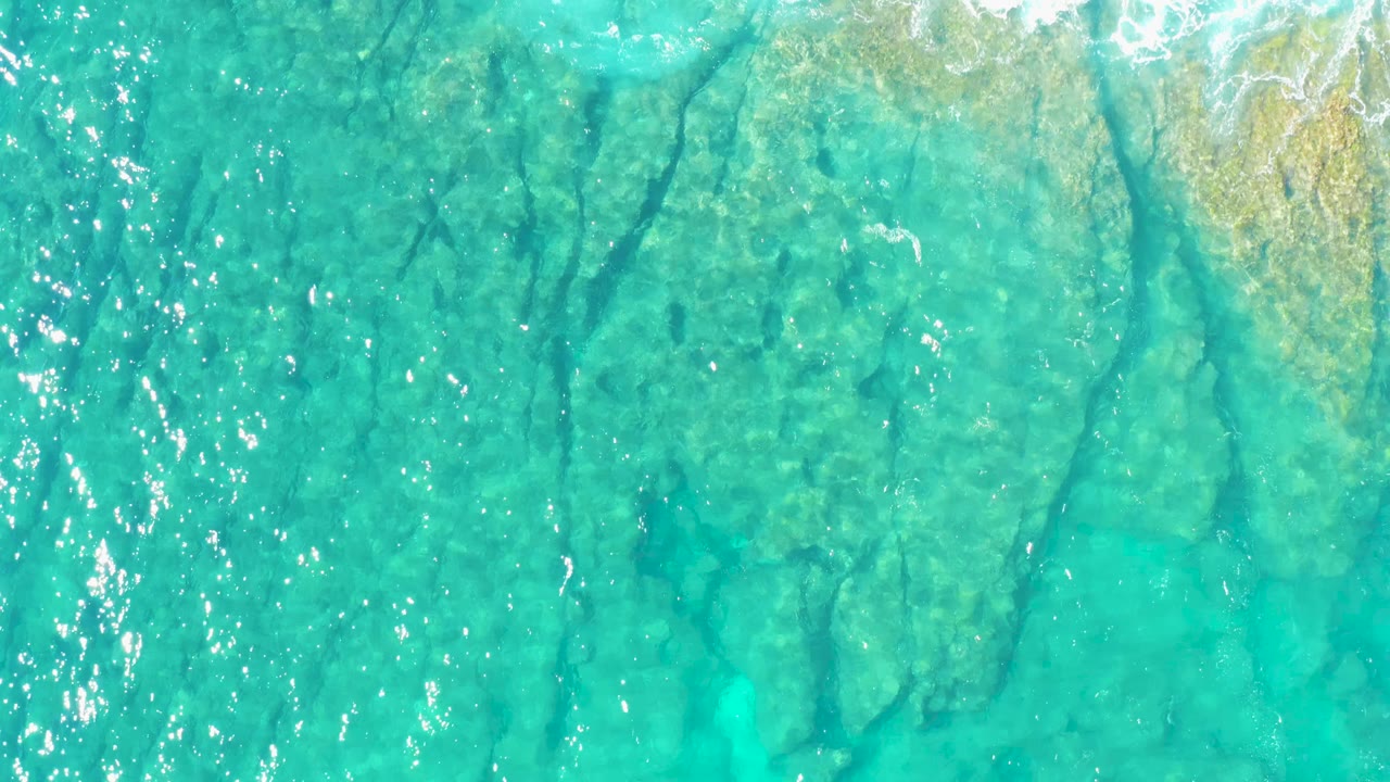 Aerial view of rippled turquoise ocean in East Cape BCS Mexico, showing dark rock fissures below the surface and no visible people.