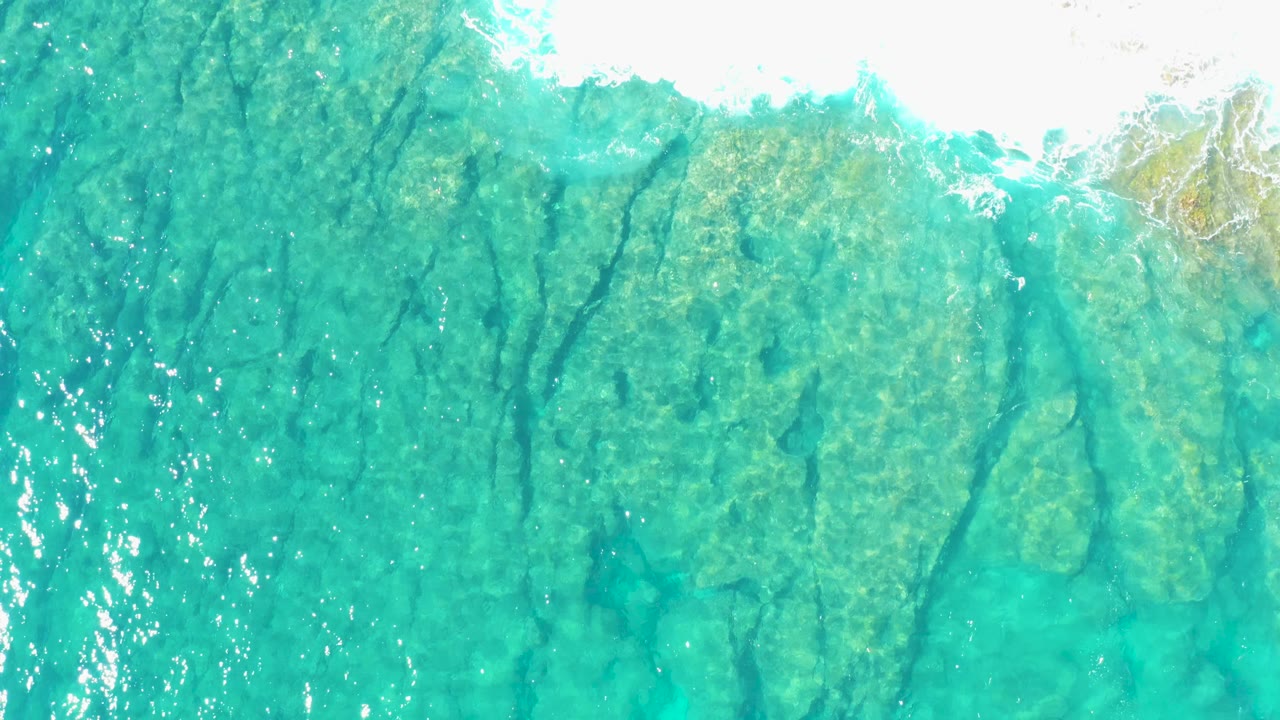 Rocky seabed visible through turquoise water with bright foam along the top.