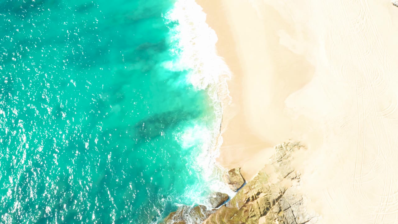 Turquoise water and foam line beside pale empty beach.