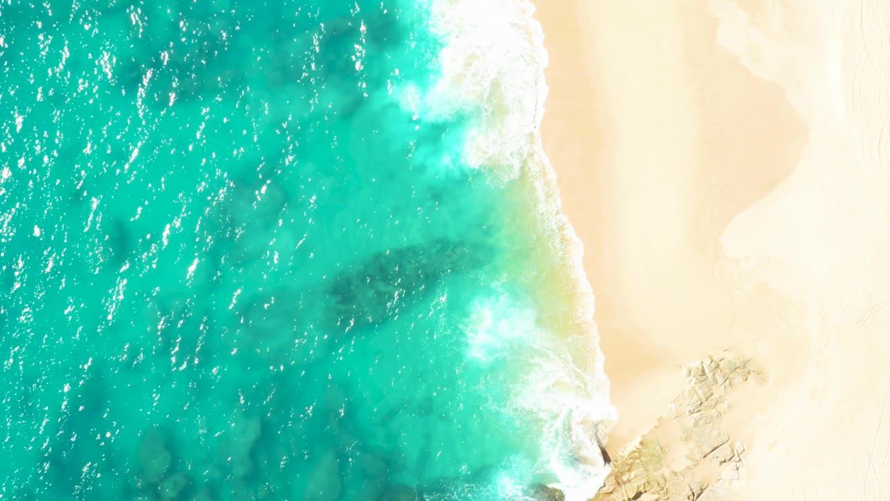 Clear turquoise water and white surf beside pale beach sand.