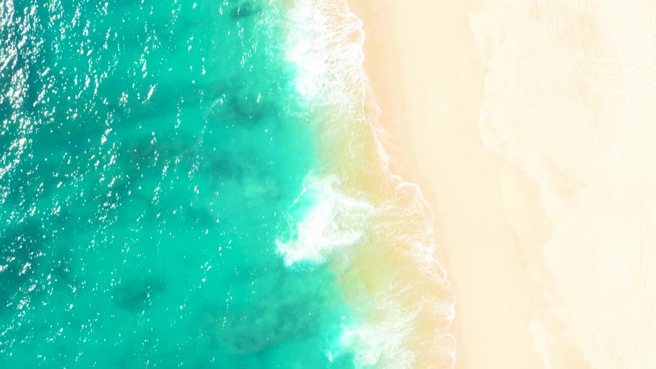 Turquoise water meets pale sand from overhead.