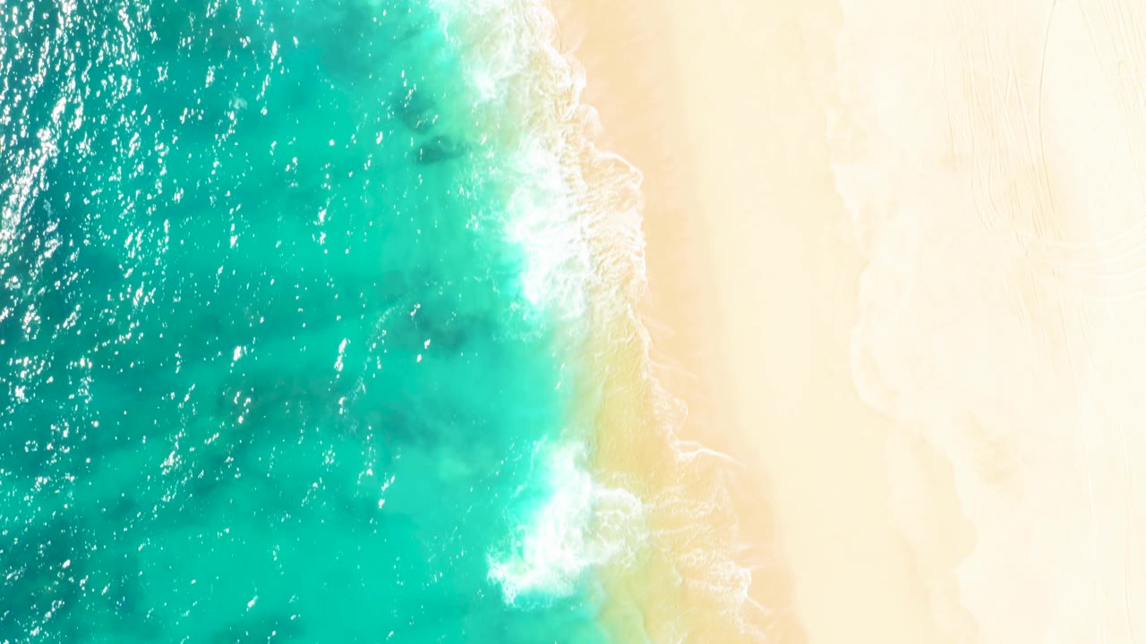 Top-down East Cape shoreline with darker patches under turquoise water, bright sand to the right, a small breaking wave near center, and no visible people.
