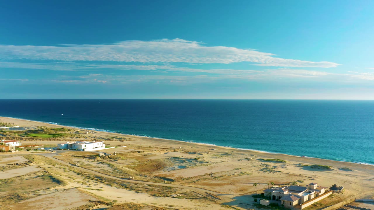 Coastal dunes and beach with ocean horizon and a white building near the shore.