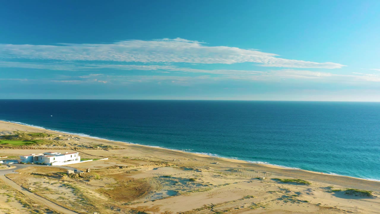 White house and sandy coastline seen from above with ocean and sky beyond.