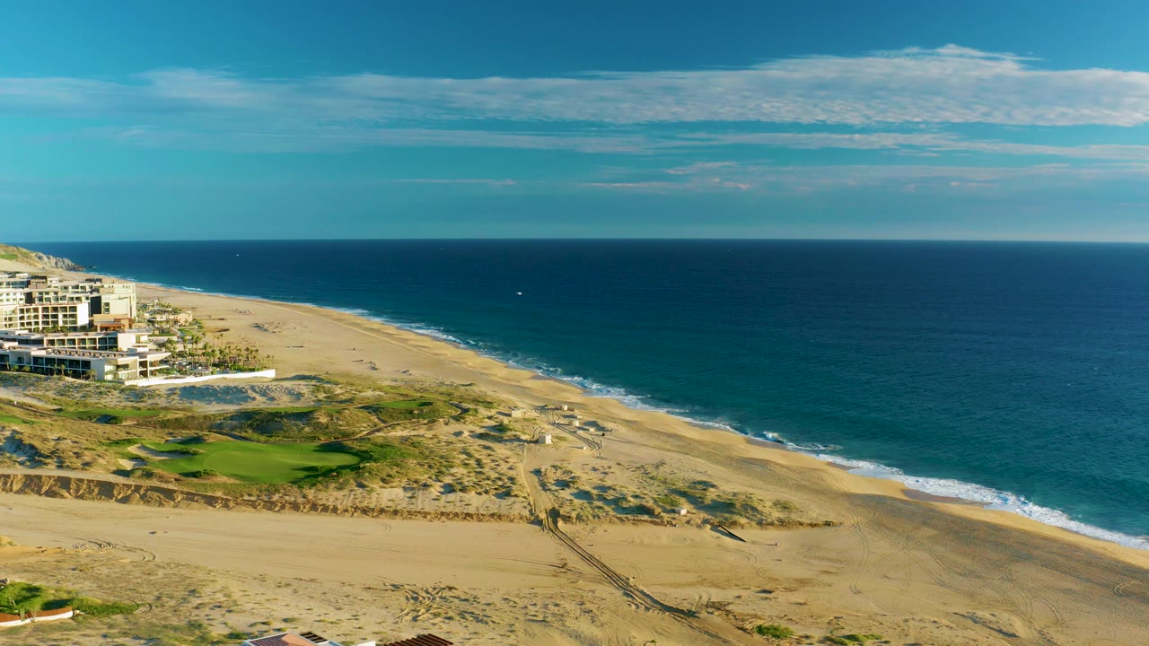 Sandy coastline from above with ocean on the right and buildings partly cropped left.