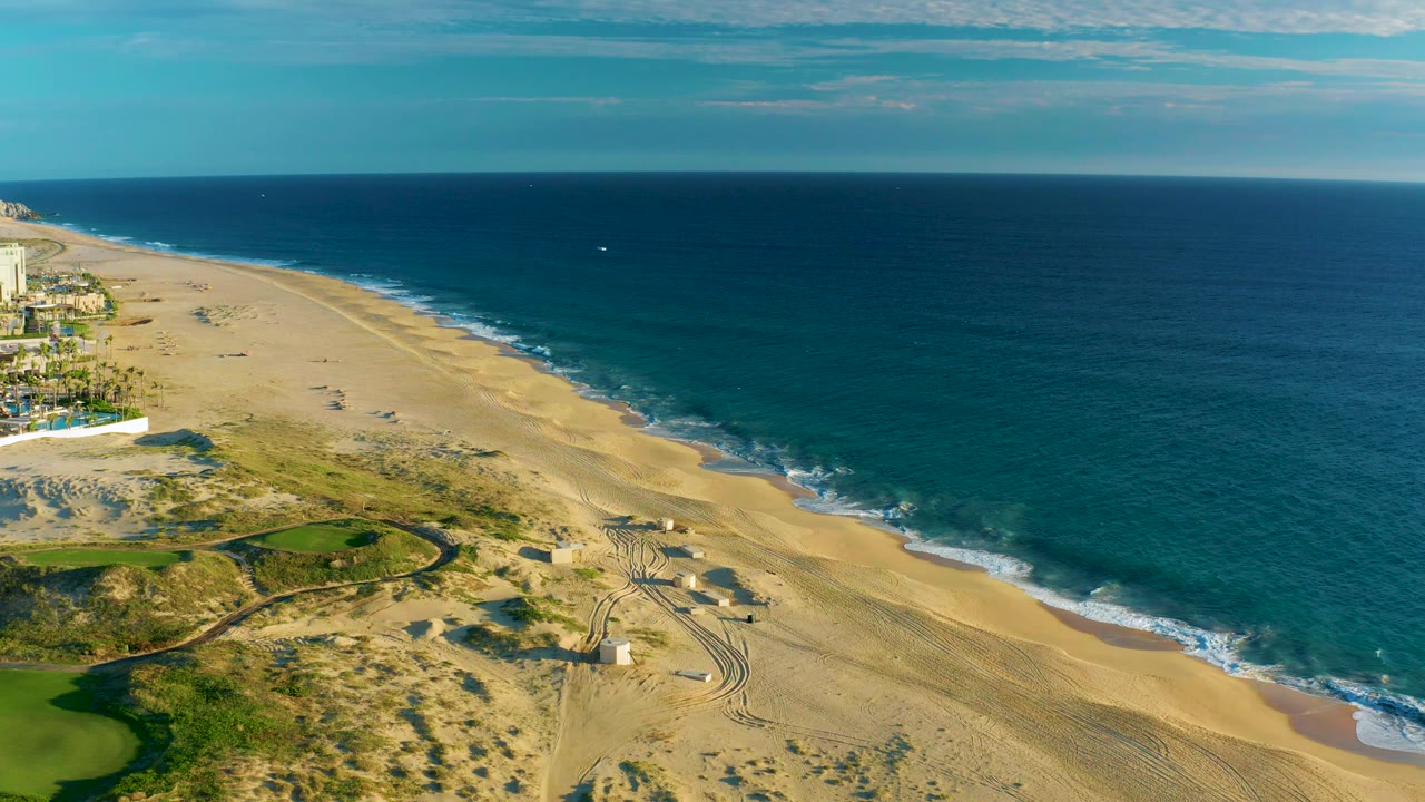 Wide aerial of beach and ocean with resort-side buildings partly visible at left