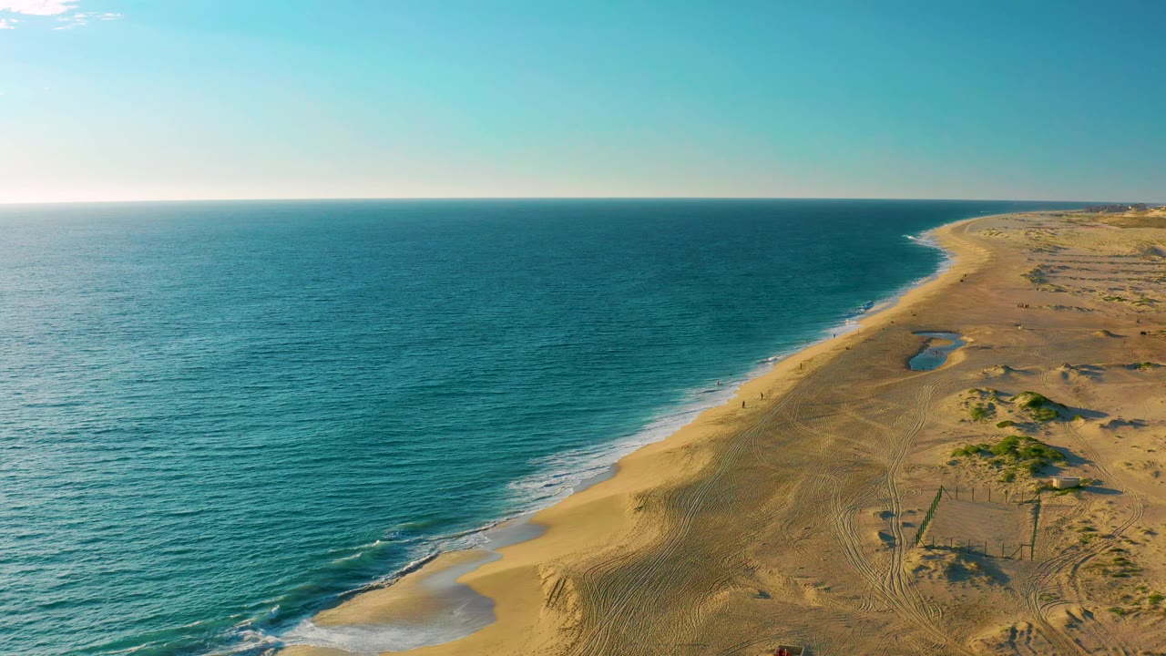 At 0:01, the Diamante Cabo San Lucas shoreline runs farther into the distance, with thin white surf on the sand, dune tracks on the right, and no visible people.