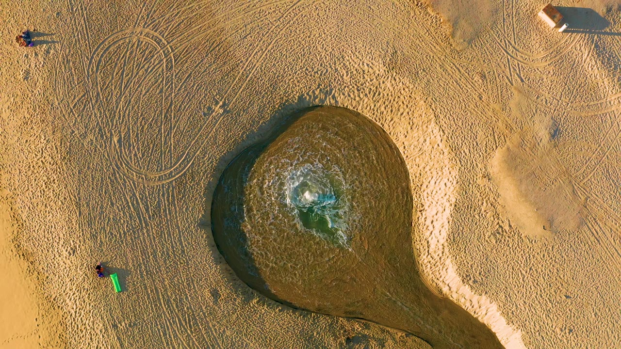 Circular wet beach pool with people and tracks seen from above.