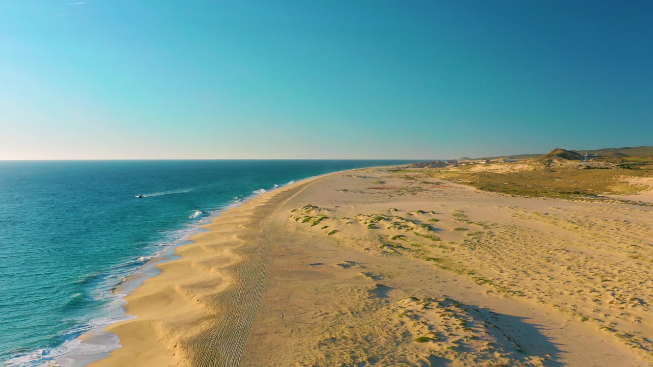 Aerial view of sandy coastline with blue ocean and dunes.