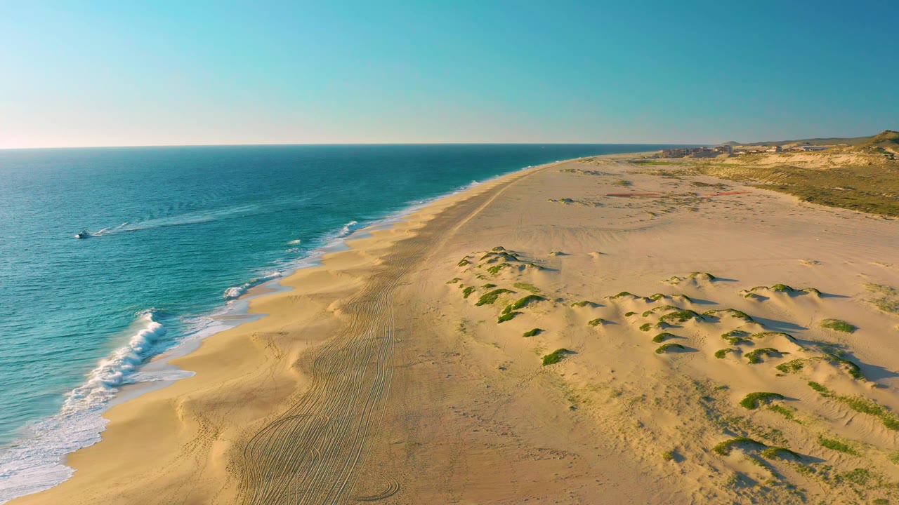 Small boat leaves a wake along the blue shoreline beside sand dunes.