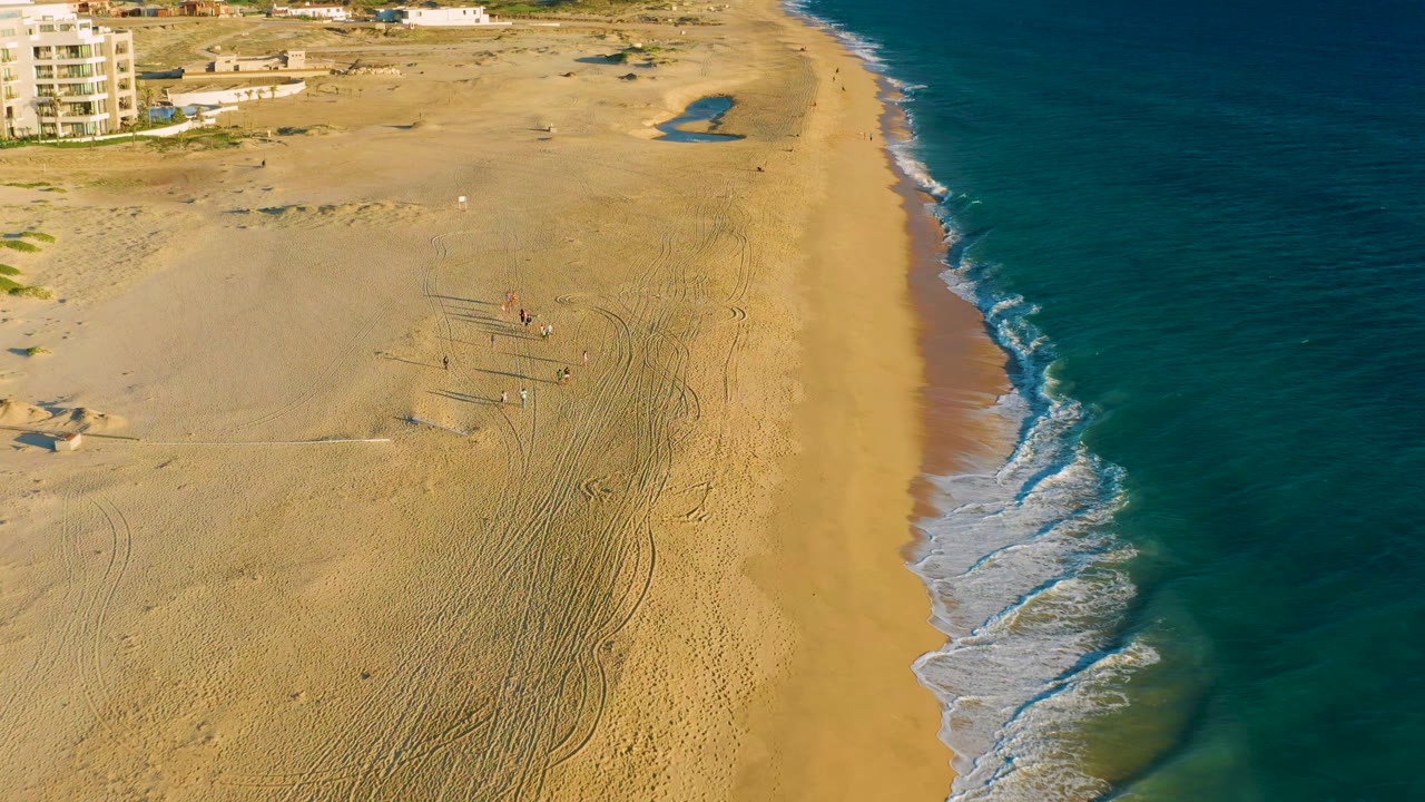 Drone view of beachgoers on sand beside the shoreline.