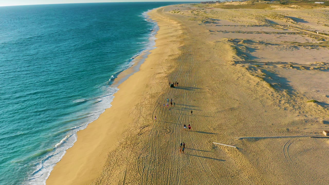 Drone view of a sandy shoreline with small groups walking near the surf