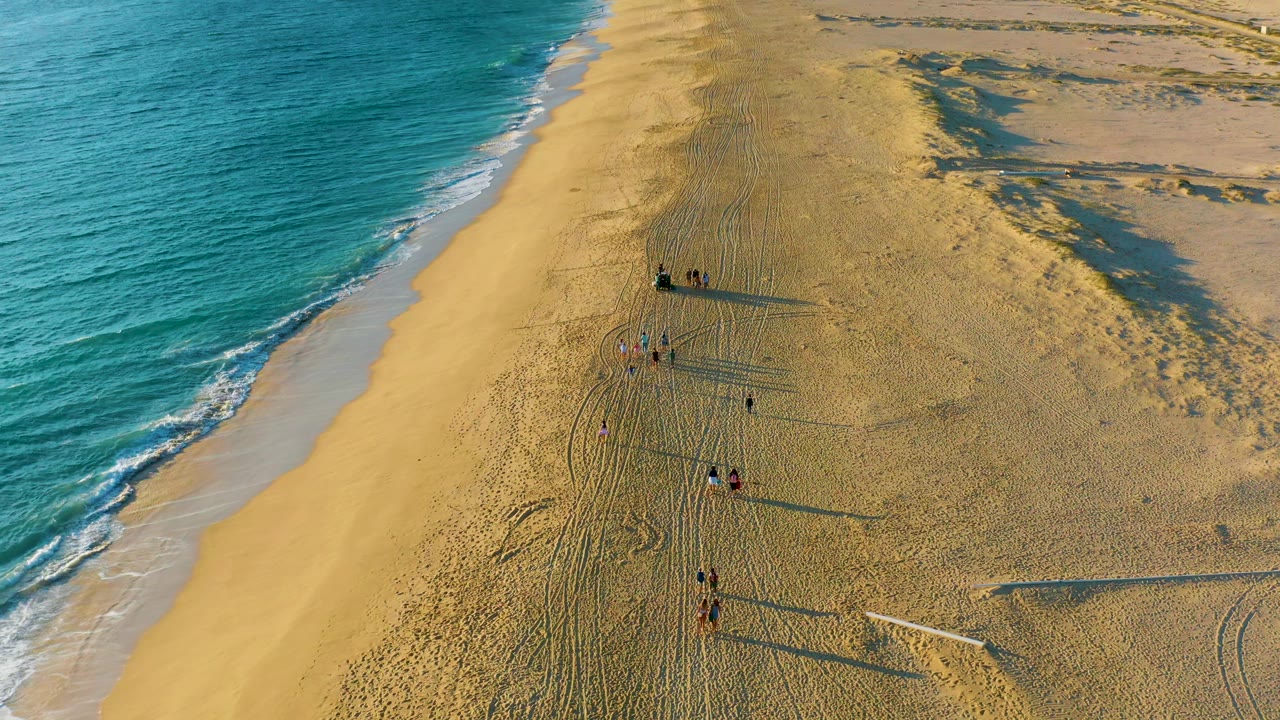 Small groups of people on a wide sandy shoreline with ocean surf at left.