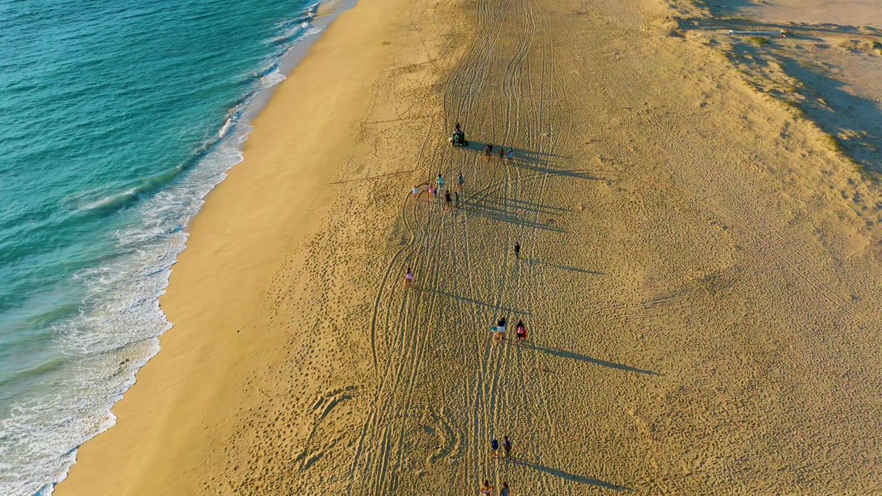 Small groups of people on sand near tire tracks and ocean waves.