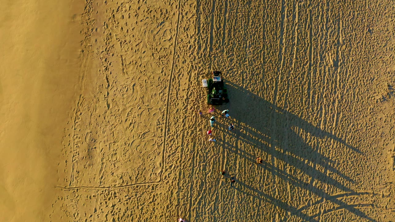 Beach cart and people viewed from above on tracked sand.