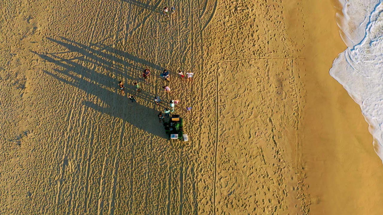 People on rippled sand beside a narrow band of breaking surf.