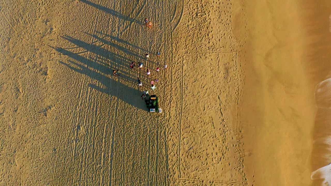 People and a vehicle on rippled beach sand near the waterline.