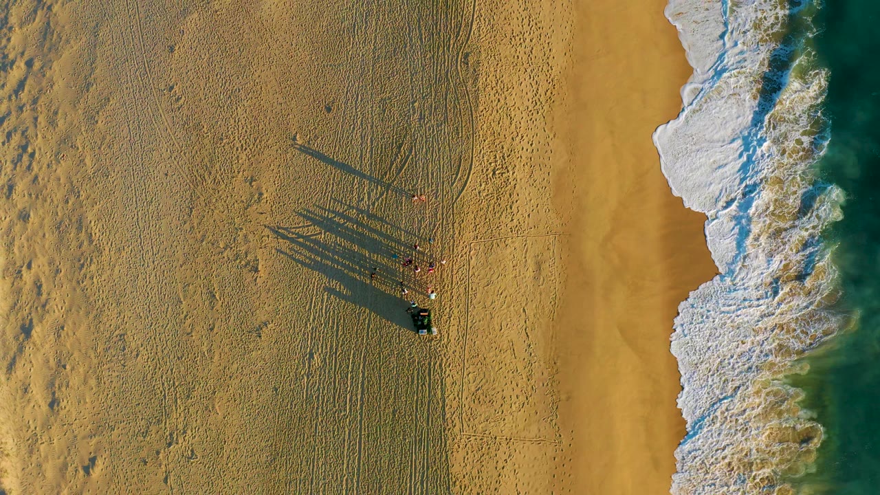 Overhead sand and surf with people casting long shadows.