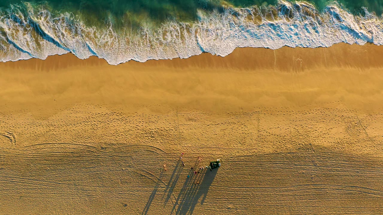 Breaking waves cover more wet sand on an empty-looking beach.