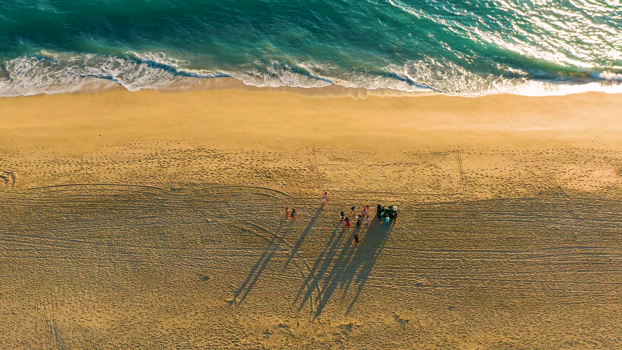 Aerial view of waves nearing shore above a small group on patterned sand.
