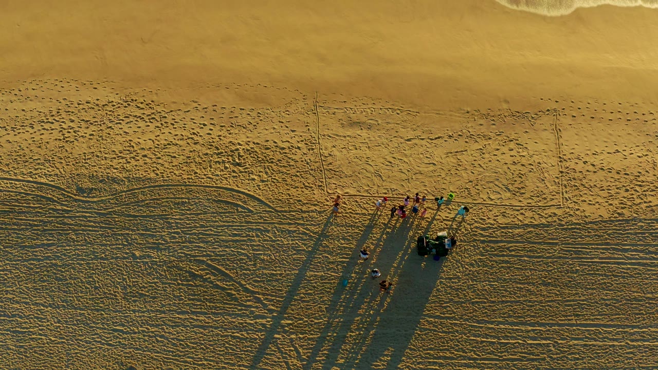 High overhead view at Diamante Cabo San Lucas shows a dune buggy towing a small group across rippled sand, with long shadows and a thin line of surf near the top.
