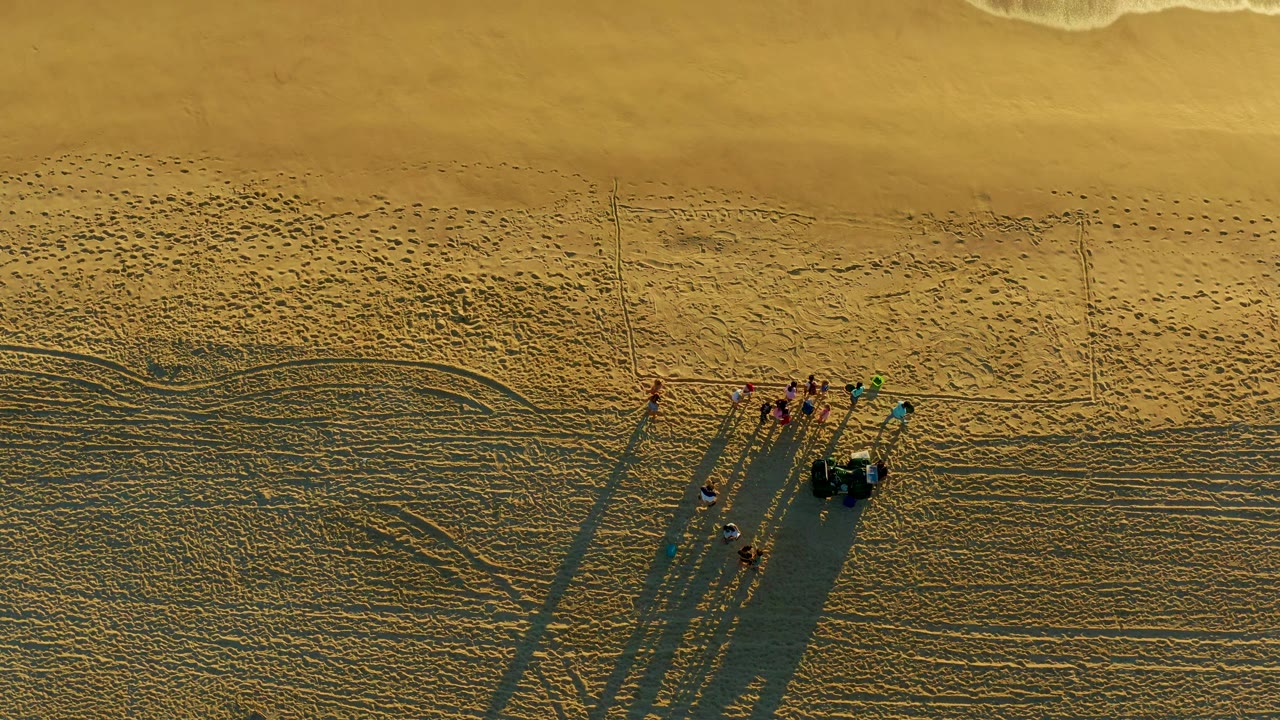 Dune buggy and people continue across open beach sand from above.
