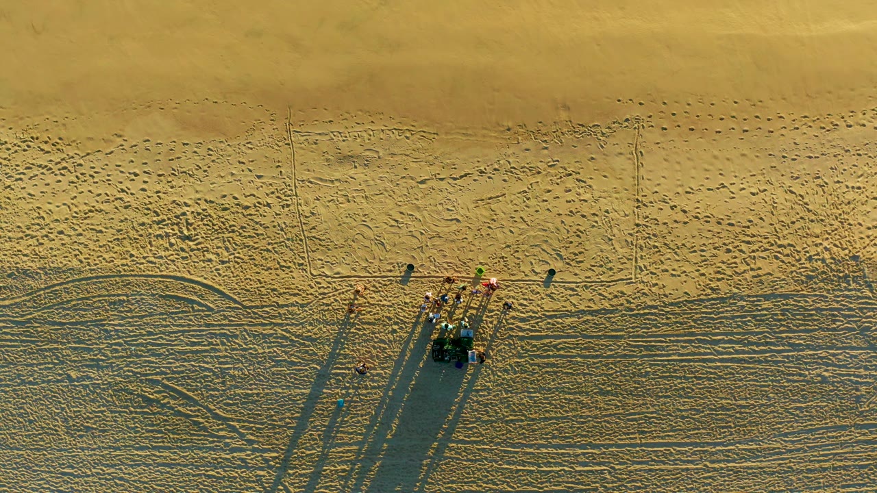 Small beach group and vehicle seen from above with footprints and tracks in sand.