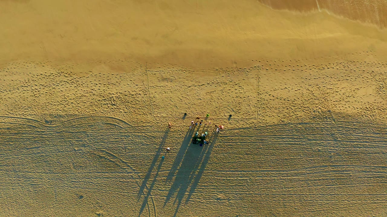 Small group on sandy beach casting long shadows.