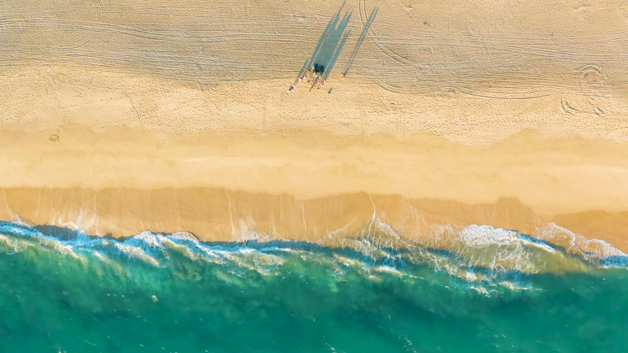 Aerial shoreline with waves breaking across pale sand.