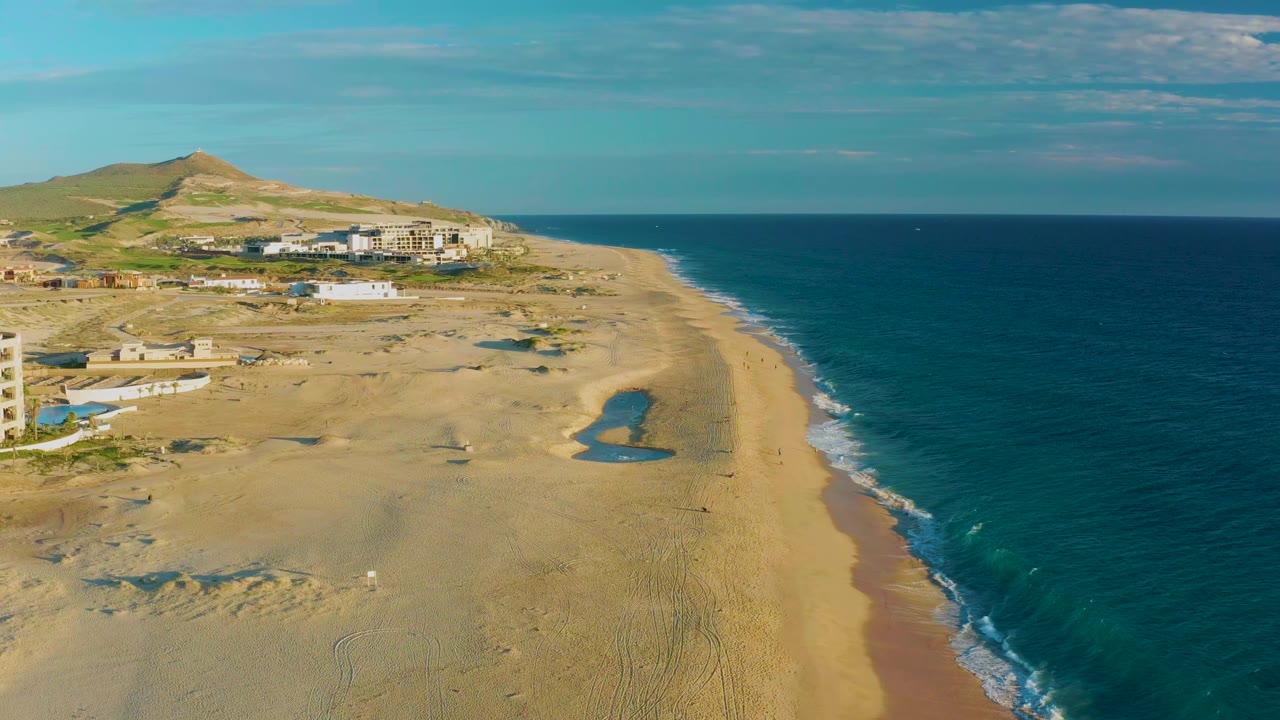 Sandy shoreline with turquoise water, dunes, coastal buildings, and clear sky.