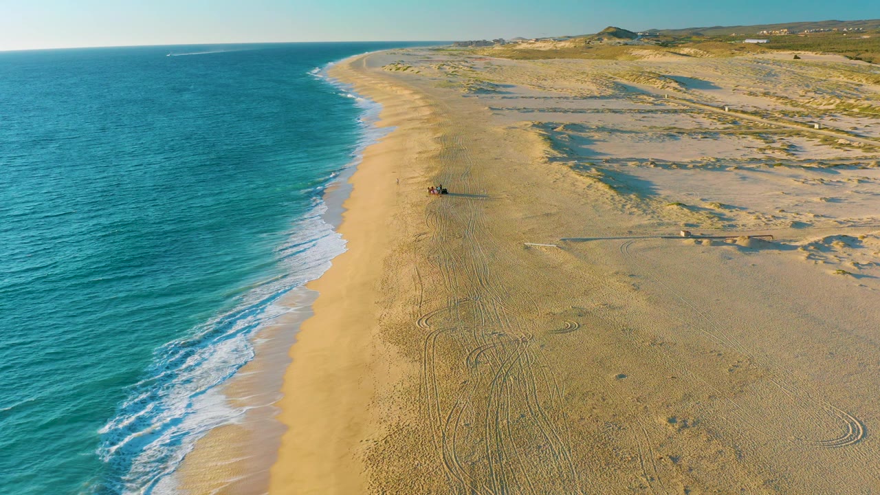 High coastal view of gentle waves and a long sandy beach.