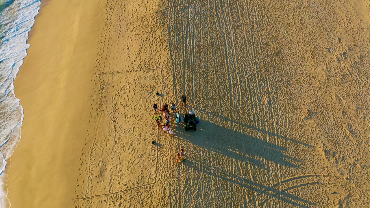 Aerial beach scene with clustered people and receding waves.