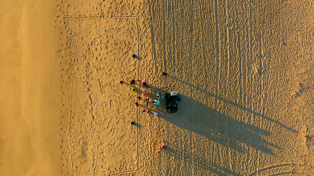 Aerial view of a small group and dune buggy casting long shadows on sand.