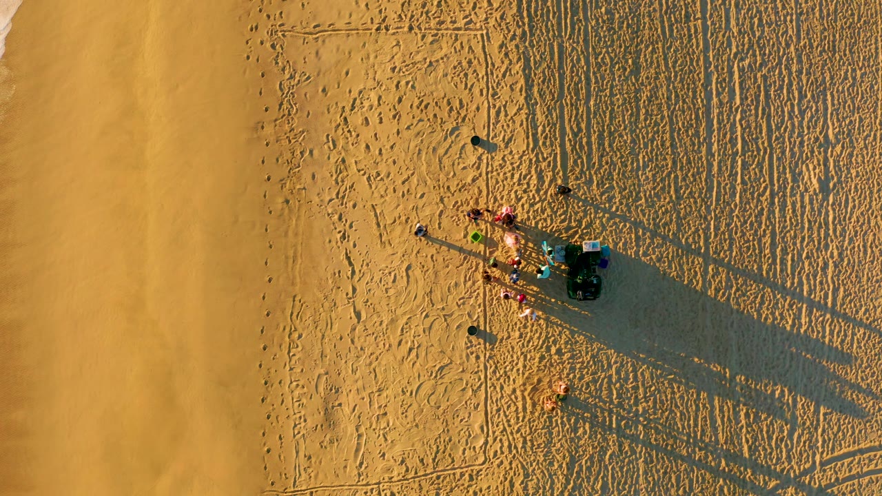 Overhead beach scene with people, sand tracks, and surf near the edge.