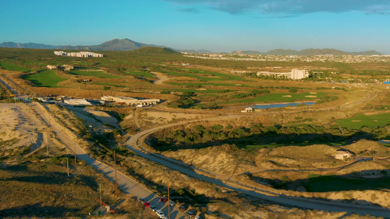 Aerial view of a road crossing dry fields with hills and buildings in the distance.