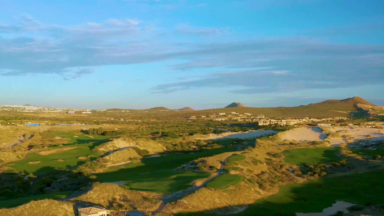 At 0:01, Diamante Cabo San Lucas appears from a high aerial angle with green fairways crossing dry ridges, distant development near the horizon, and no visible people.