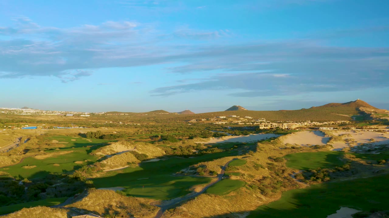 At 0:01, the Diamante Cabo San Lucas aerial view holds on green fairways, pale dry slopes, a water channel, distant development, layered hills, and no visible people.
