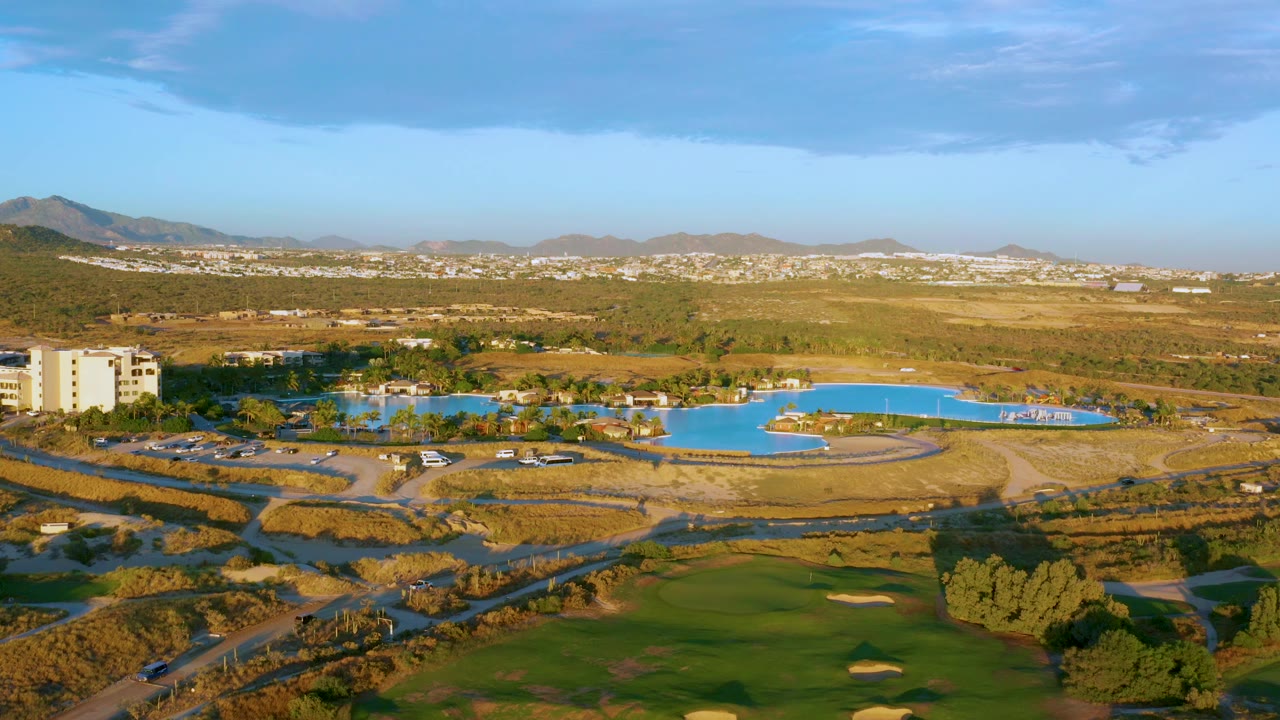 Golf course foreground with blue water feature, roads, building, and dry hills beyond.