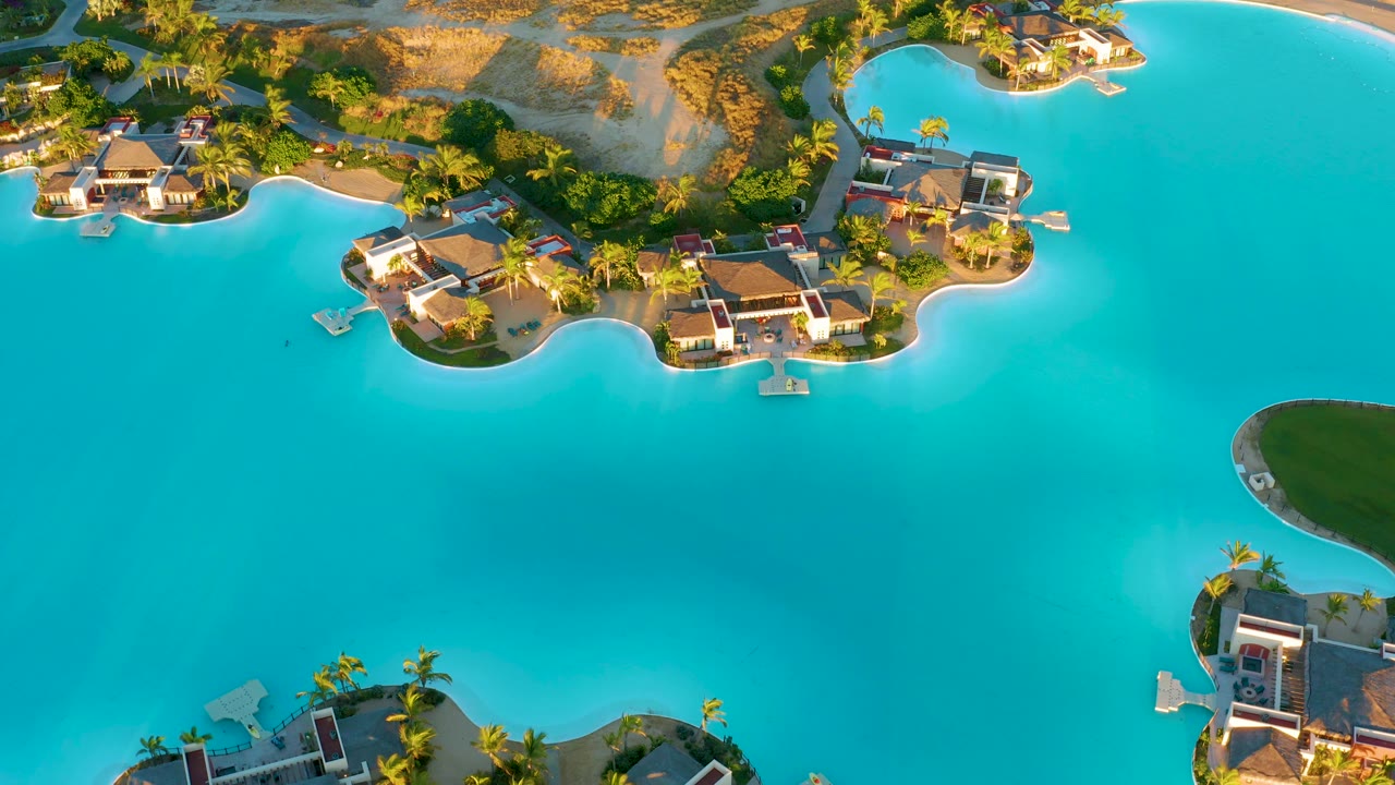 Aerial lagoon scene with villas, curved islands, palm trees, and open water.