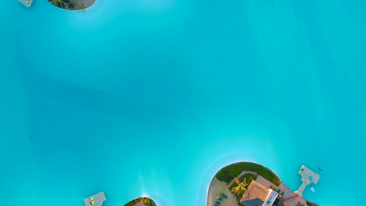Overhead view in Diamante Cabo San Lucas of bright turquoise water with partial resort edges, small dock structures, and no visible people.