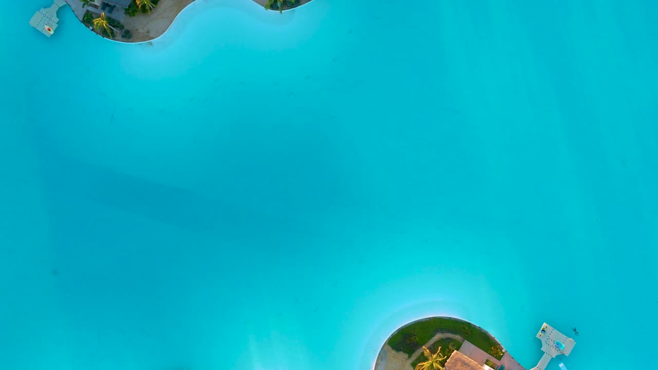 Near-vertical aerial frame in Diamante Cabo San Lucas showing broad turquoise water, curved resort shoreline sections, small docks, and no visible people.